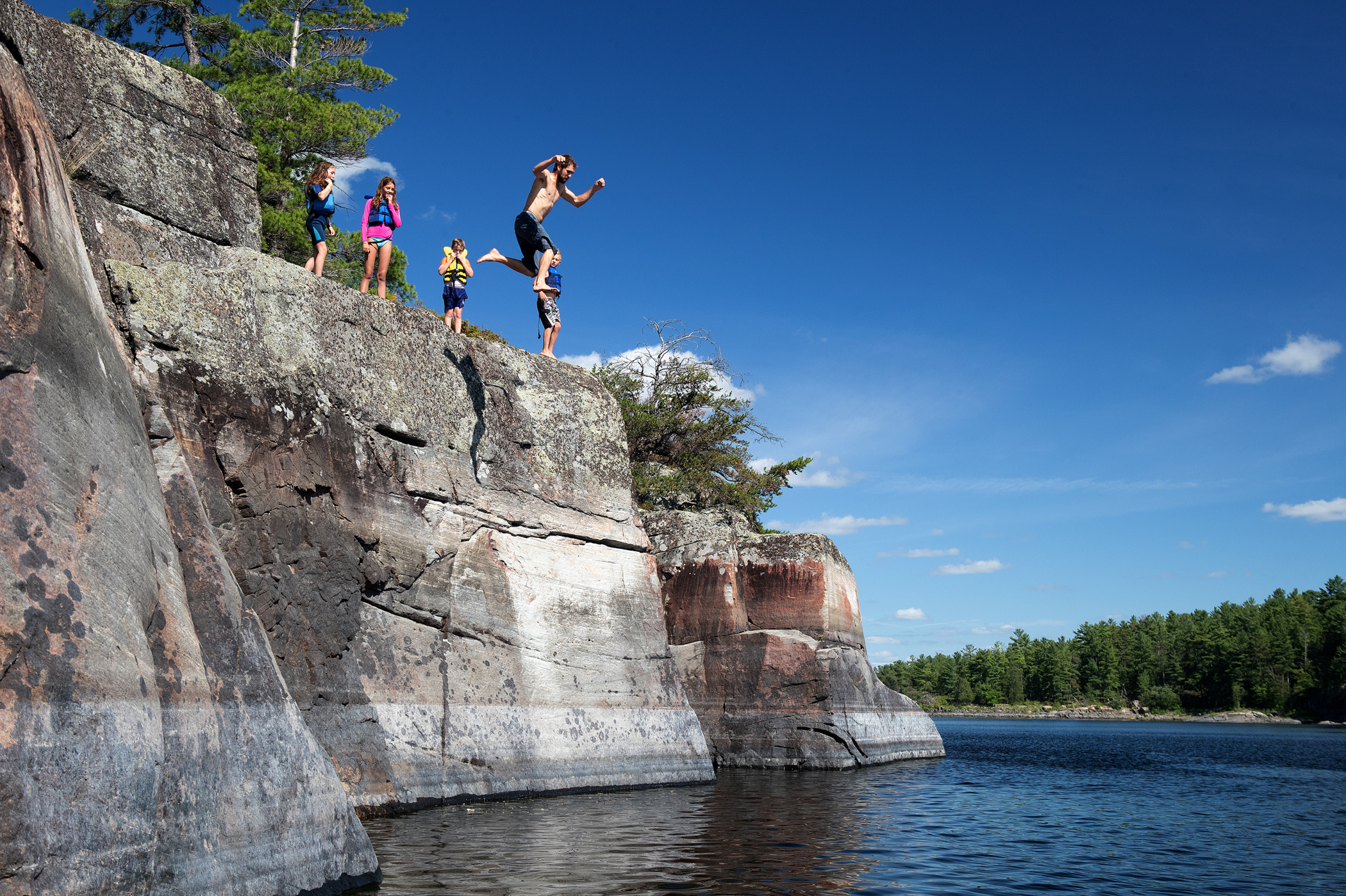 friends jumping off rocks into a river